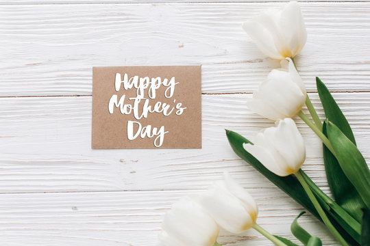 happy mothers day text sign on stylish craft greeting card and tulips on white wooden rustic background. flat lay with flowers and gift blank paper with space for text. greeting card