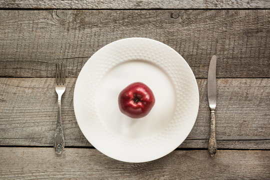 Table set with red apple on white plate with knife and fork.