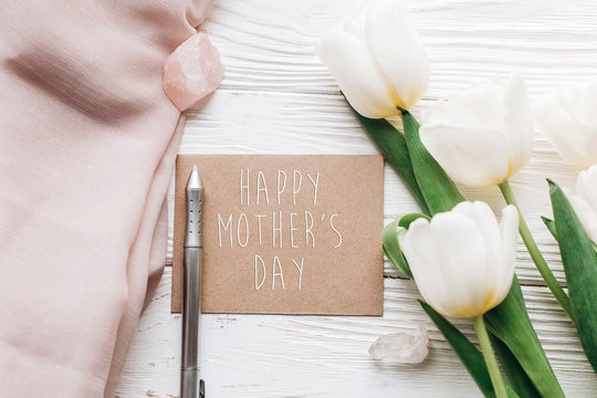 happy mothers day text sign on stylish greeting card template with tulips and crystals and pen on white wooden rustic background. flat lay. photo workshop. space for text.