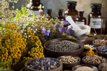 Herbs, berries and flowers with mortar, on wooden table background