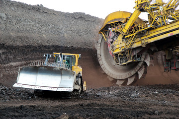 bulldozer and huge mining excavator wheel in brown coal mine