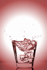 Ice cubes splashing into glass, ice cube dropped into glass of water, fresh, cold water, isolated on rose, pink, red background.
