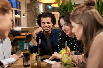 happy friends with drinks and bill at bar or cafe