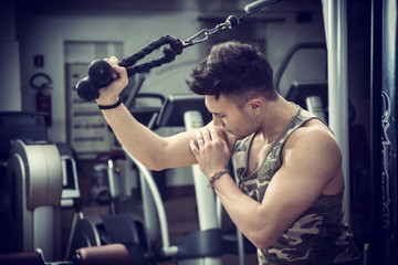 Young man training on gym equipment, pulling handle on cables