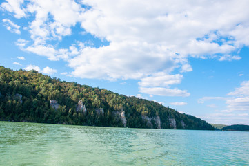 Forest on the bank of the lake . White clouds reflect in the water