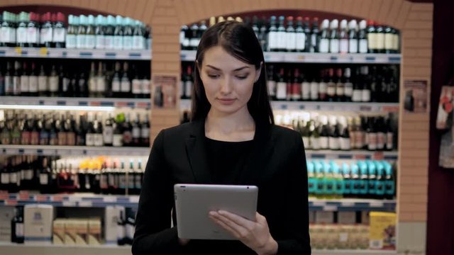 Cosultant in wine shop, oman in the store choosing wine according check list or information in tablet computer