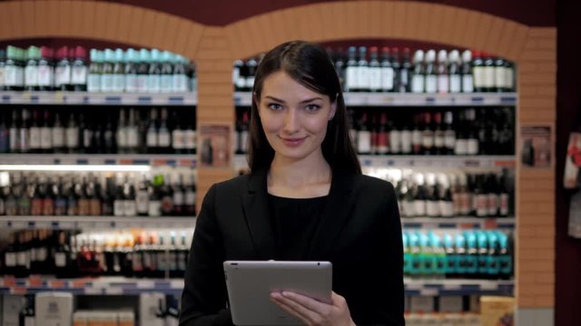 Cosultant in wine shop, oman in the store choosing wine according check list or information in tablet computer