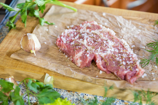 Fresh raw pork steak with salt and spices on paper. Fresh green dill and parsley.  Shallow depth of field. Coloring and processing photo.
