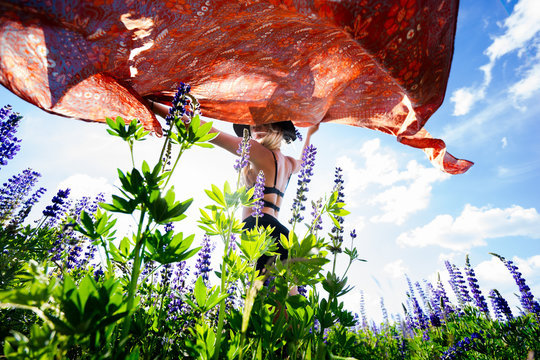 Woman holding sheet above head in field with wildflowers