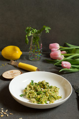 Quinoa with courgette and green peas. Gray background, white plate and tulips.