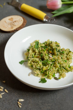 Quinoa with courgette and green peas. Gray background, white plate and tulips.