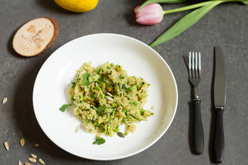 Quinoa with courgette and green peas. Gray background, white plate and tulips.