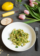 Quinoa with courgette and green peas. Gray background, white plate and tulips.