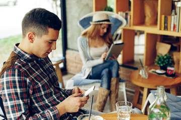Young man texting on the phone with a woman in the background