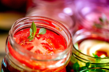 Canning fresh tomatoes with onions for winter in jelly marinade. A shot of basil leaves on top of a red ripe tomato slices and onion rings being put in jar.

