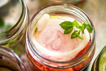 Canning fresh tomatoes with onions for winter in jelly marinade. A shot of basil leaves on top of a red ripe tomato slices and onion rings being put in jar.

