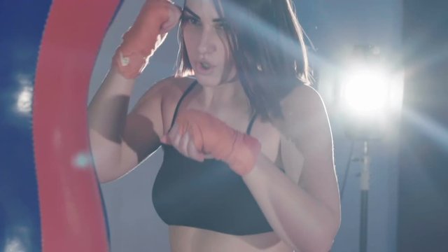 Pretty kickboxing woman training punching bag in sport studio. Slowly