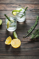 Alcoholic drink gin tonic cocktail with lemon, rosemary and ice on rustic wooden table.