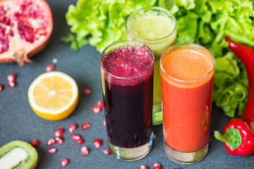 three glasses of different fresh juice. Beet, carrot and kiwi juices on grey background