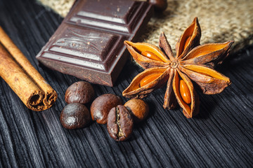 Chocolate bar and spices on wooden table, close up