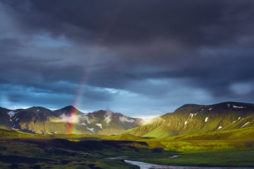 Travel to Iceland. Beautiful sunset in camping near Alftavatn lake. Icelandic landscape with mountains, sky and clouds. Trekking in national park Landmannalaugar. Rainy Evening with big rainbow.