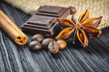 Chocolate bar and spices on wooden table, close up