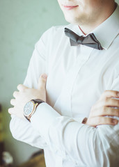 Young man in white shirt and watch standing crossing hands