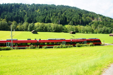 grüne Landschaft mit rotem Regionalzug bei Mittenwald in Bayern
