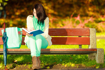 Woman reading book sitting on bench in park