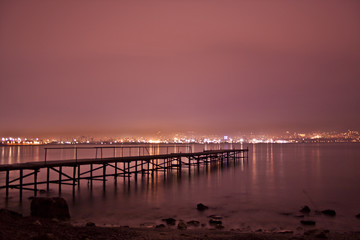 Fototapeta na wymiar City night lights with red sky, sea and pier