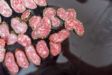 Sliced sausage with spices on black plate