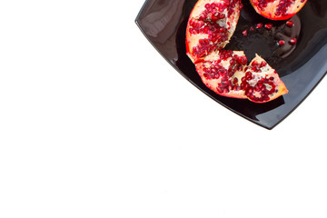 Broken red ripe pomegranates in black plate on white background