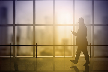 Fototapeta na wymiar Business man using a mobile while walking a office building corridor. Sun flare. Empty copy space for Editor's content.