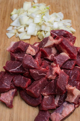 Fresh raw chopped meat beef and chopped white onion on an wooden cutting board.