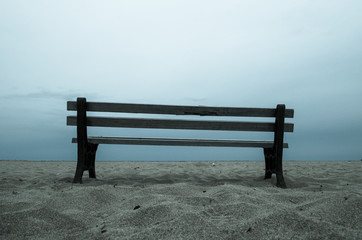 Fototapeta na wymiar Old empty bench stands on sandy beach at a dull evening, Malia, Crete, Greece