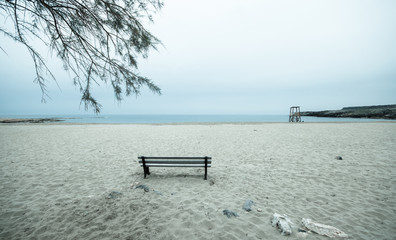 Fototapeta na wymiar Old empty bench stands on sandy beach at a dull evening, Malia, Crete, Greece