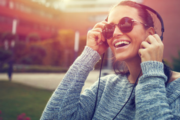 Happy young woman listening music outdoor by headphones in sunset