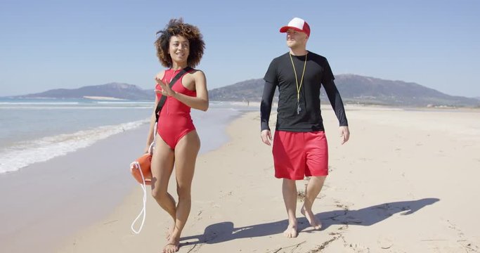 Female and male lifeguards walking along beach with orange rescue float. Tarifa beach. Provincia Cadiz. Spain. 