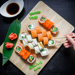 Japanese food. Sushi rolls, sauce and woman hand with chopsticks on black background. Flat lay. Top view.
