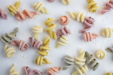 Curly and twisted pasta shapes on a cutting board in various colors of pink, yellow, green and white