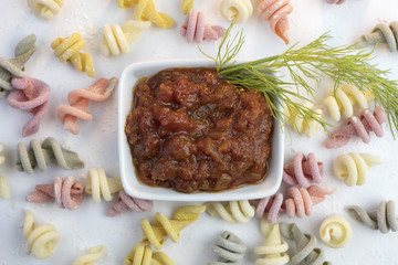 Curly and twisted pasta shapes on a cutting board in various colors of pink, yellow, green and white