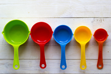 Colorful measuring spoons for kitchen on a white wooden background - obrazy, fototapety, plakaty