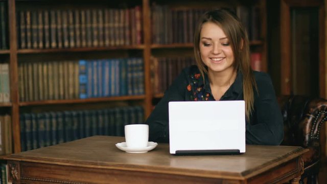 Young smiling woman with laptop computer at the library talks with friends via web cam indoors