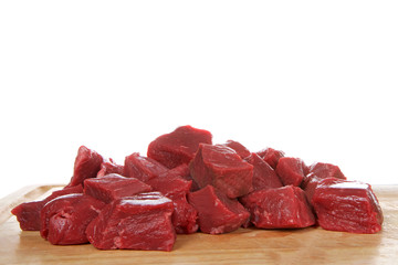 Fresh chopped beef steak chunks on wood chopping board, isolated on white background
