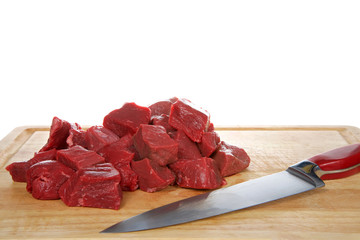 Fresh chopped beef steak chunks on wood chopping board with knife laying in front of meat, isolated on white background