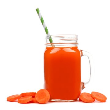 Mason jar glass of carrot juice with straw and surrounding carrot slices isolated on a white background
