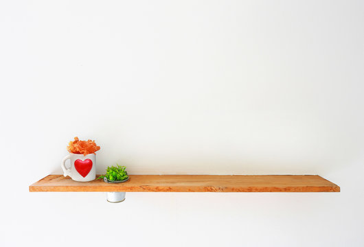 Wooden shelf on white wall with green plant and mug heart.