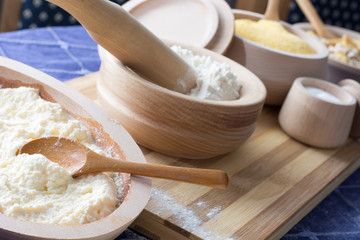 Fototapeta premium Wheat flour in the wooden bowl with spoon on the home table.