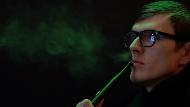 Young man in glasses smoking a hookah in a cafe