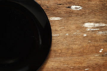 The black color plate put on the hard wood surface texture background represent the kitchenware...